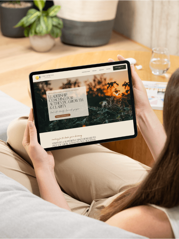Woman on a couch holding a tablet showing Earth Wise Coaching homepage – custom coaching website design by Sprout Marketing and Design in Chandler, AZ