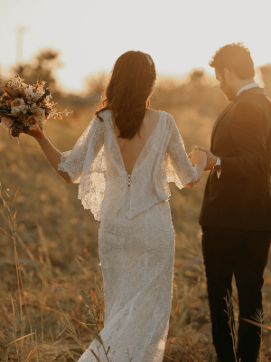 Bride and groom walking through a field at sunset