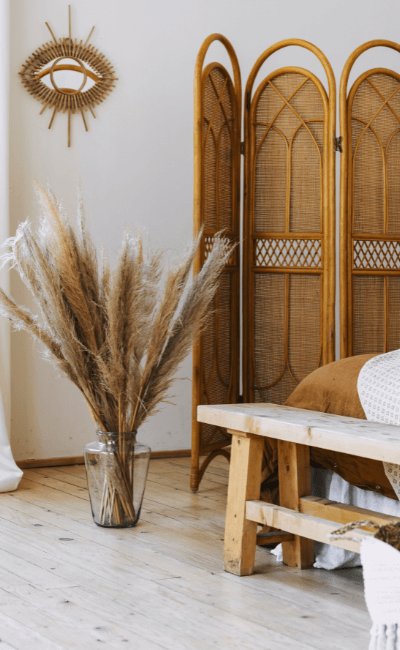 Bedroom corner with a rattan screen, pampas grass and a rustic wood bench