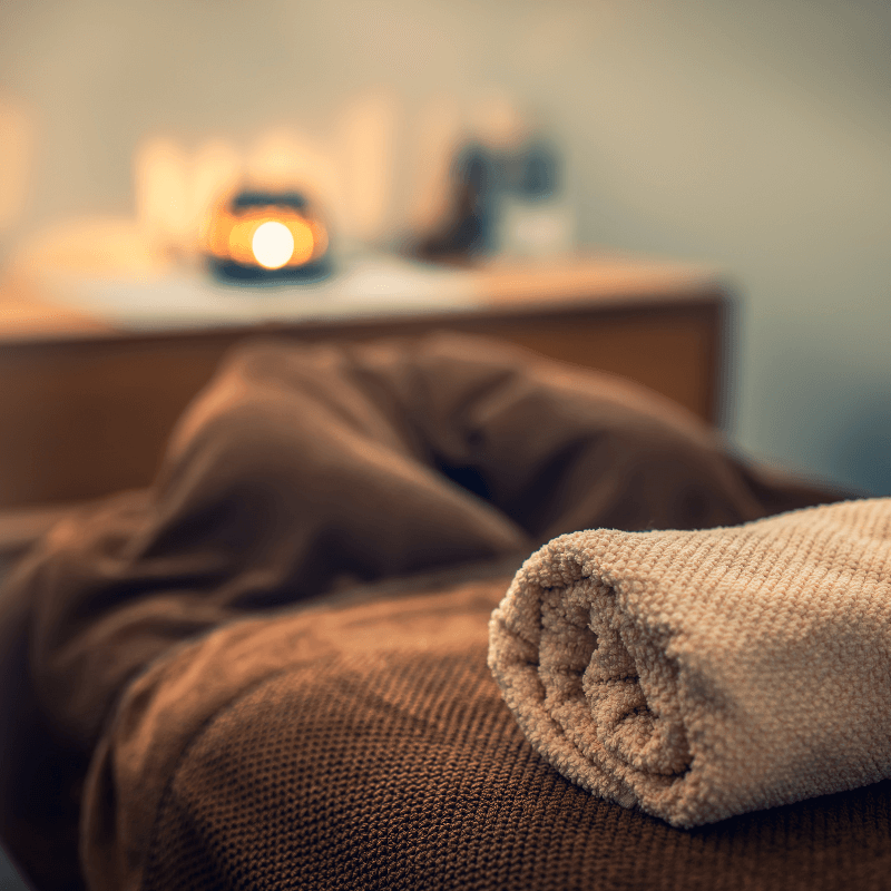 Folded towels and a lit candle beside the massage table