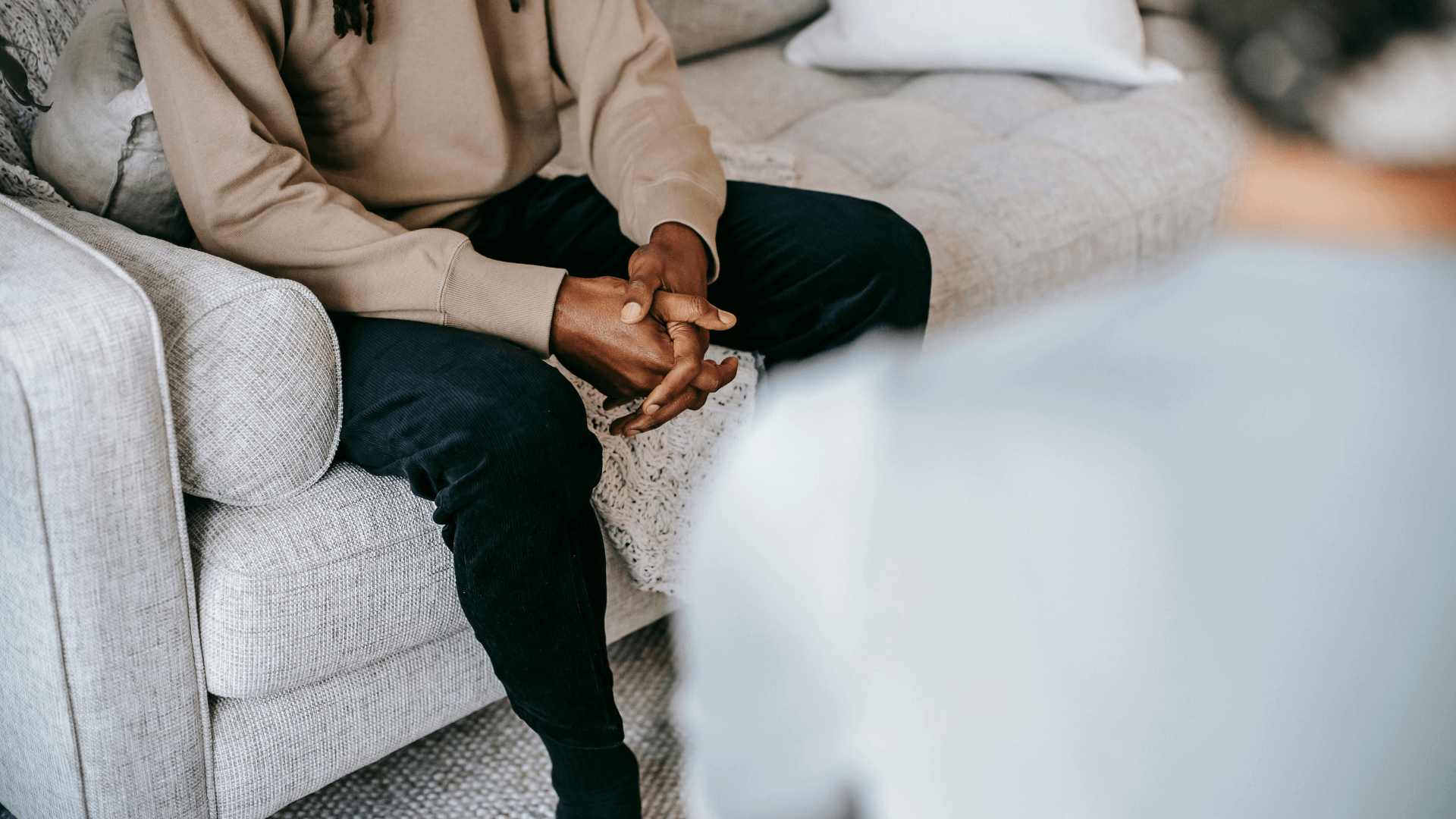 Person sitting on a gray sofa with hands clasped during a therapy session