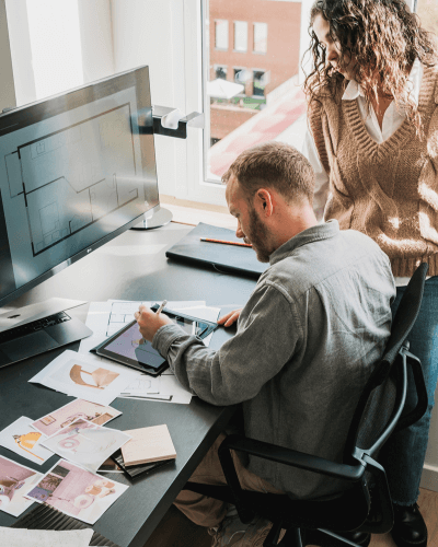 Project manager reviewing a floor plan at a computer with a designer