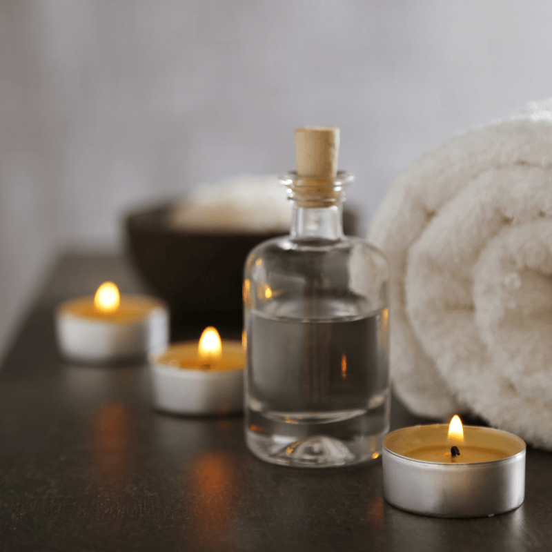 Glass bottle of massage oil with candles and folded towels