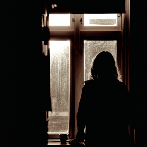 Silhouette of a person standing by a window in a dim room