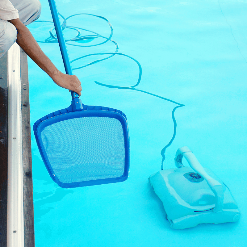 Pool technician skimming leaves from a backyard pool