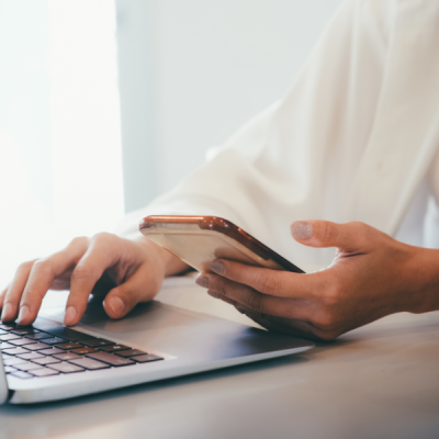 Person holding a phone in one hand and typing on a laptop with the other, representing multitasking with Google resources, featured in Sprout Marketing and Design’s blog post, ‘3 Must Have Google Resources for Service Business Owners